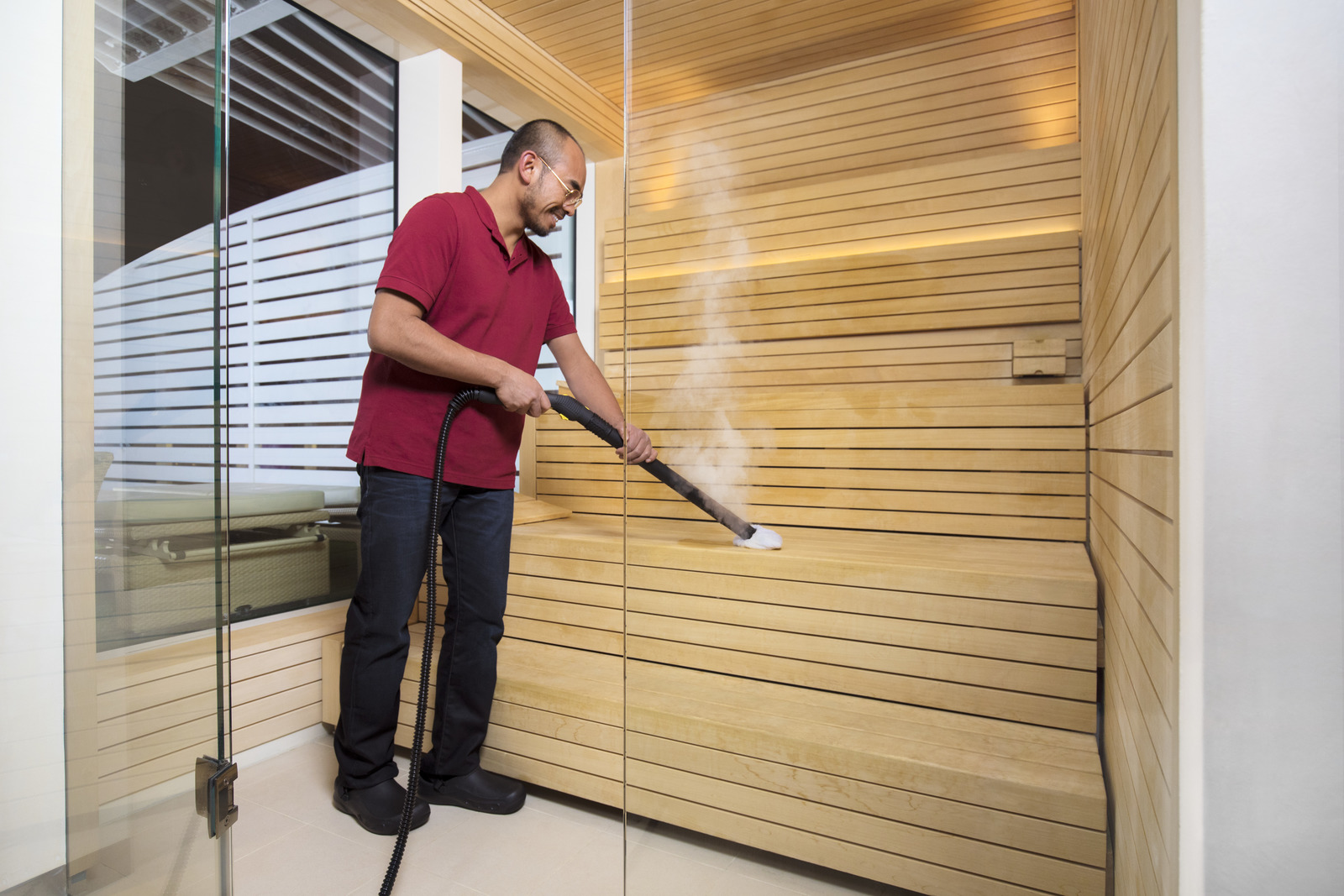 Mężczyzna czyści drewniane ławki w saunie parownicą.