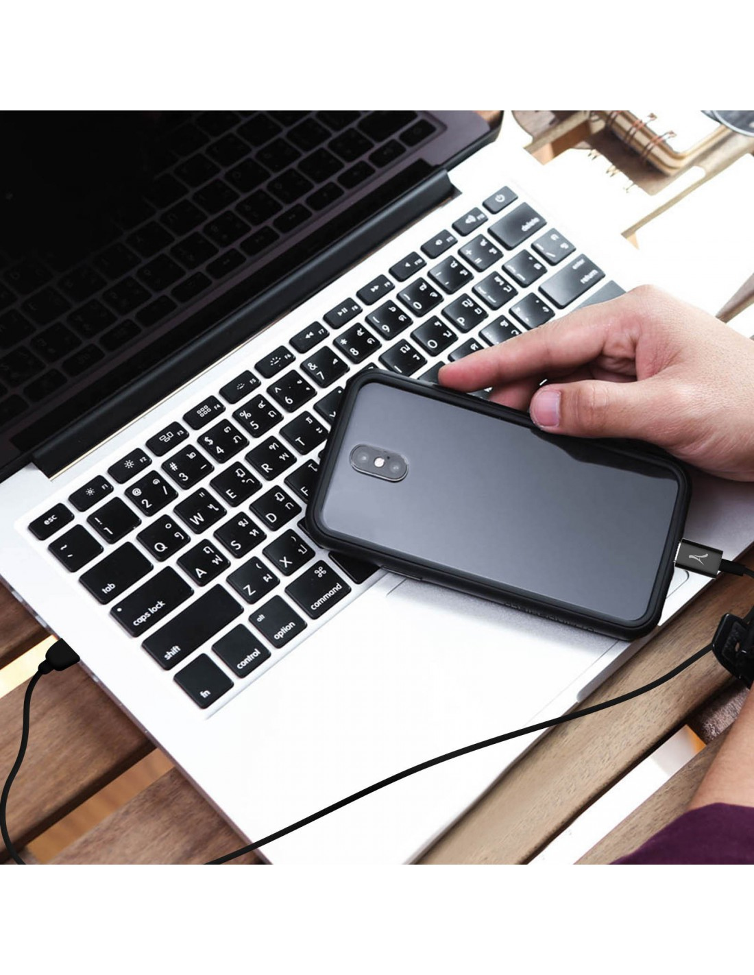 Una mano appoggia un telefono sulla tastiera di un laptop, collegato via cavo.