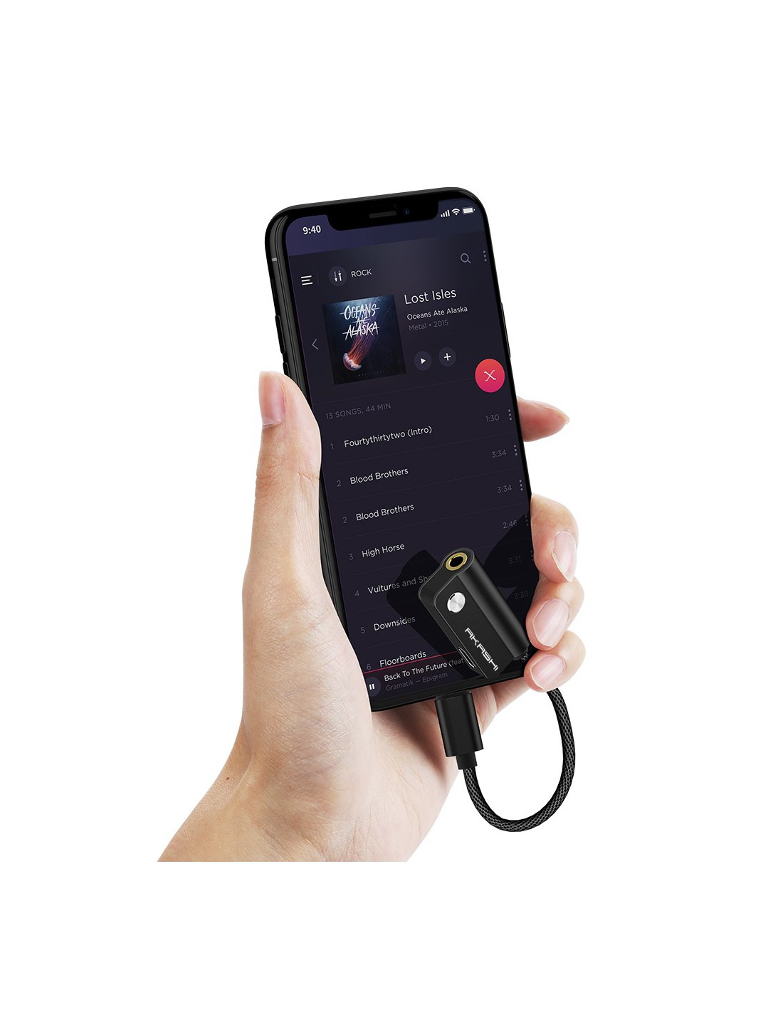 Une main tient un smartphone affichant une application musicale avec un adaptateur noir connecté.