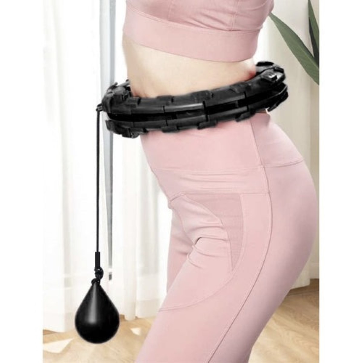 Una persona con ropa deportiva rosa usa un hula hoop inteligente negro con pesa.