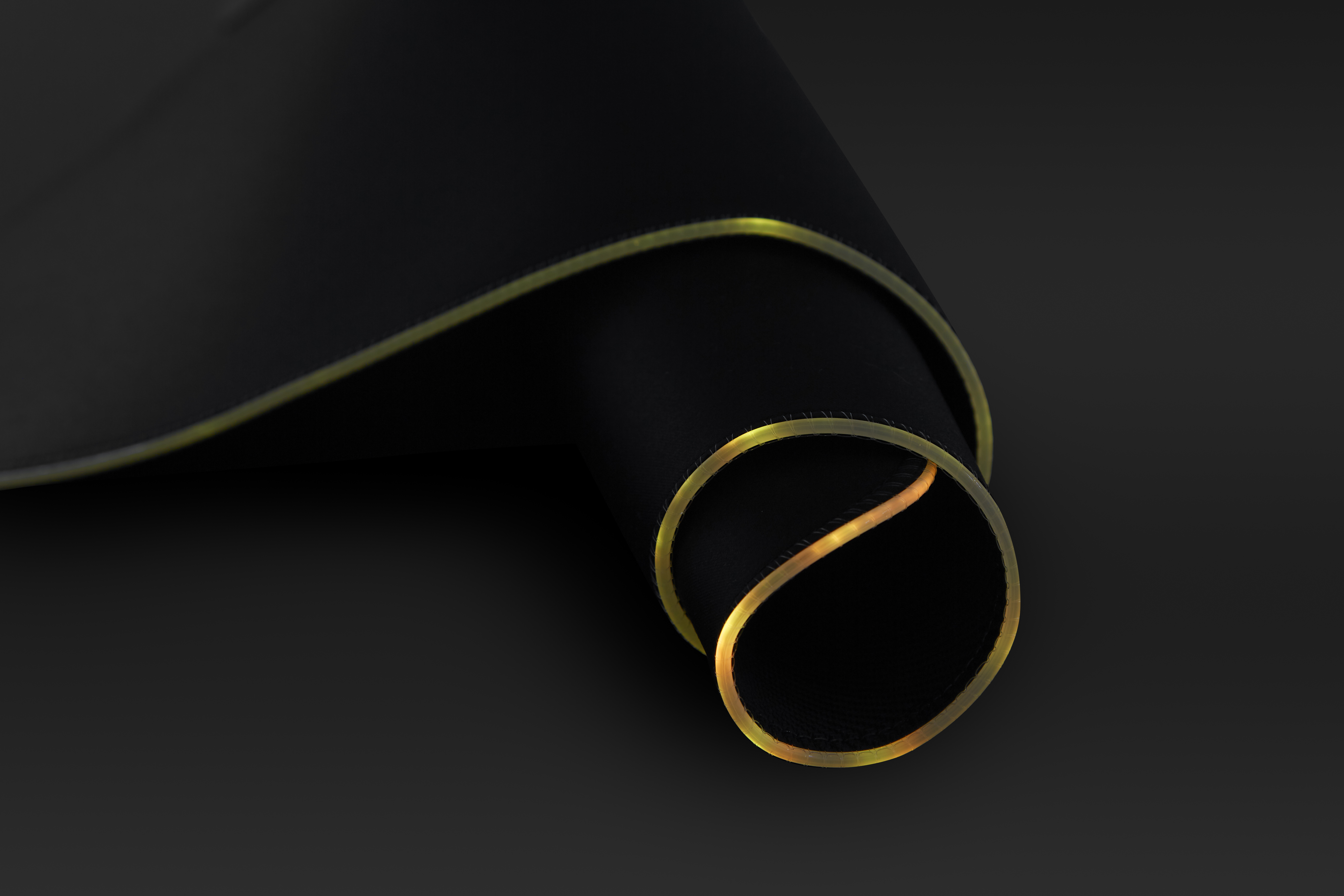 Czarna zwinięta mata z lśniącą żółtą krawędzią na ciemnym tle.