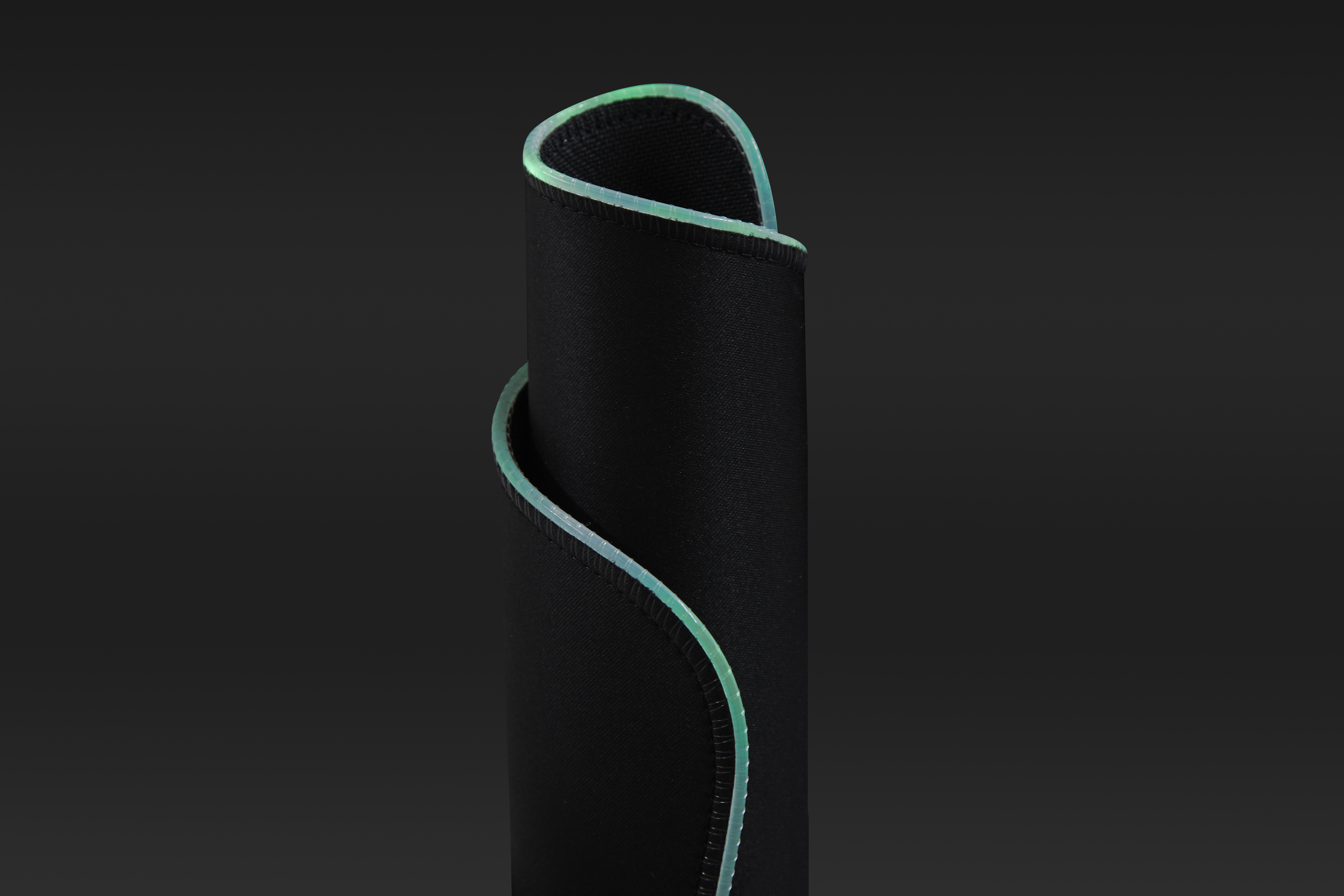 Czarna podkładka pod mysz z jasnozieloną szytą krawędzią, zwinięta na ciemnym tle.