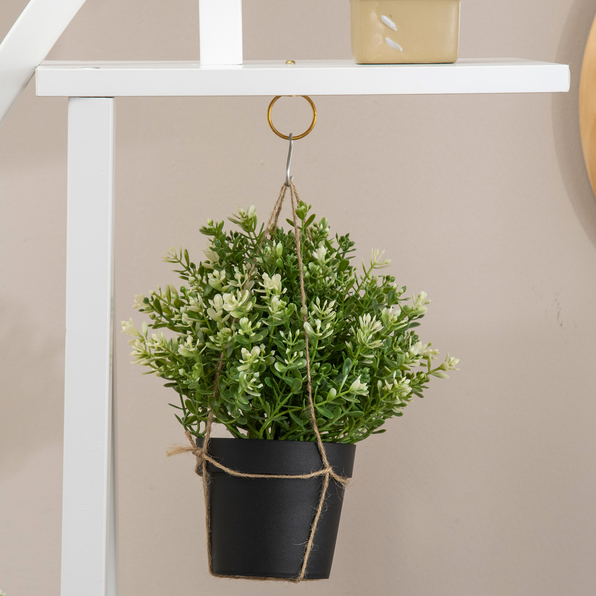 Una pianta verde con fiori bianchi pende in un vaso nero da una mensola bianca.