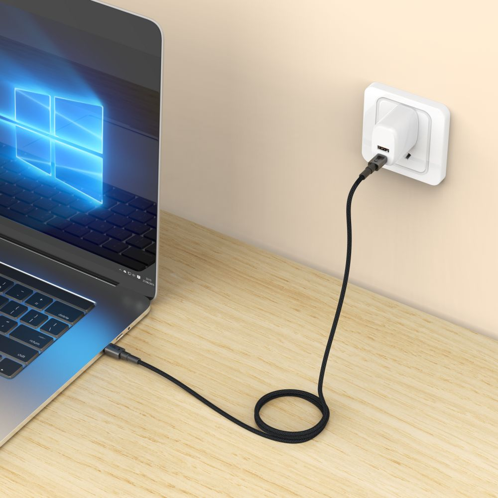 A laptop is charging via a black USB-C cable plugged into a white wall socket.