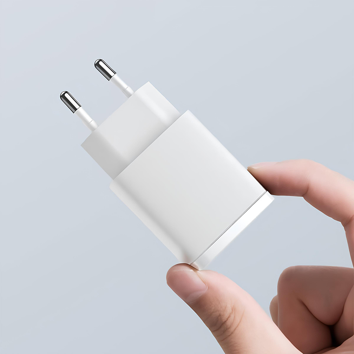 Dłoń trzyma biały adapter z dwoma srebrnymi bolcami.