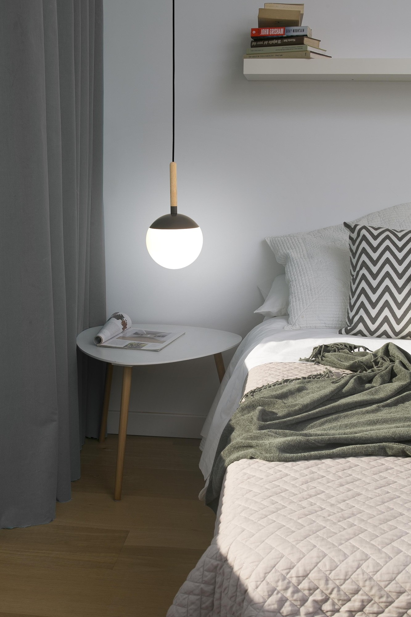 Una camera da letto moderna con lampada a sospensione, tavolino e letto con coperta verde.