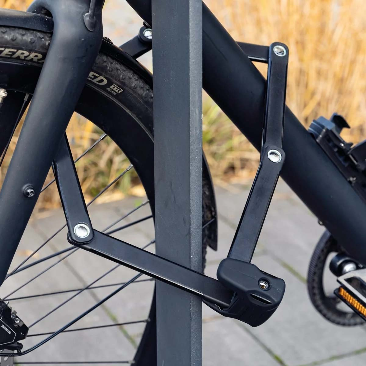 Ein schwarzes Faltschloss sichert ein Fahrrad an einem Pfosten.