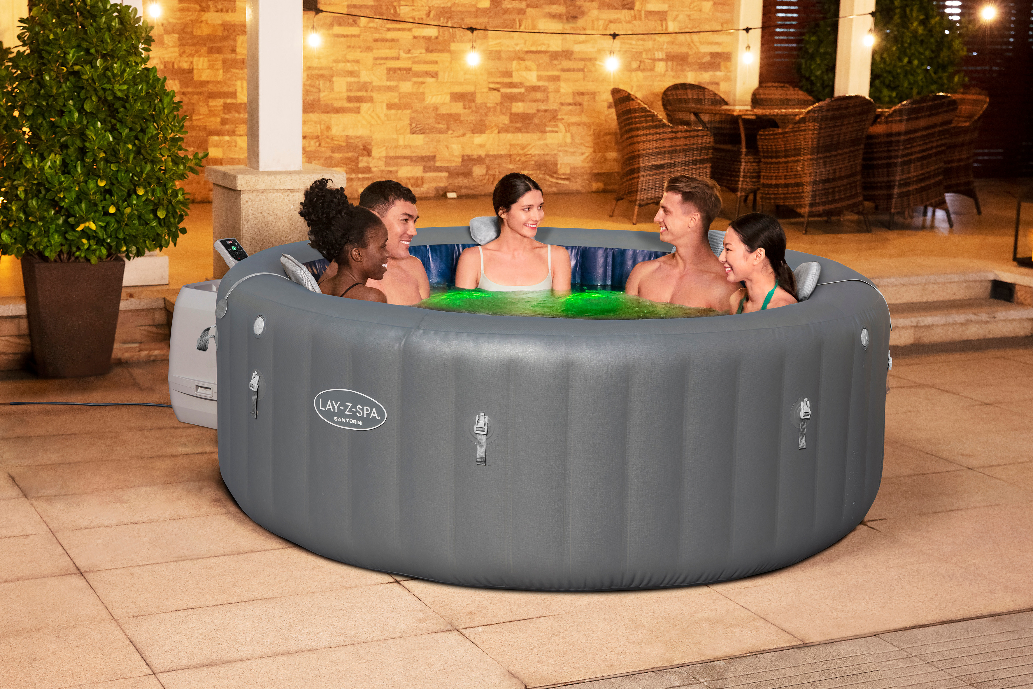 Sechs Personen entspannen sich in einem aufblasbaren Whirlpool bei Nacht, beleuchtet von Lichterketten.