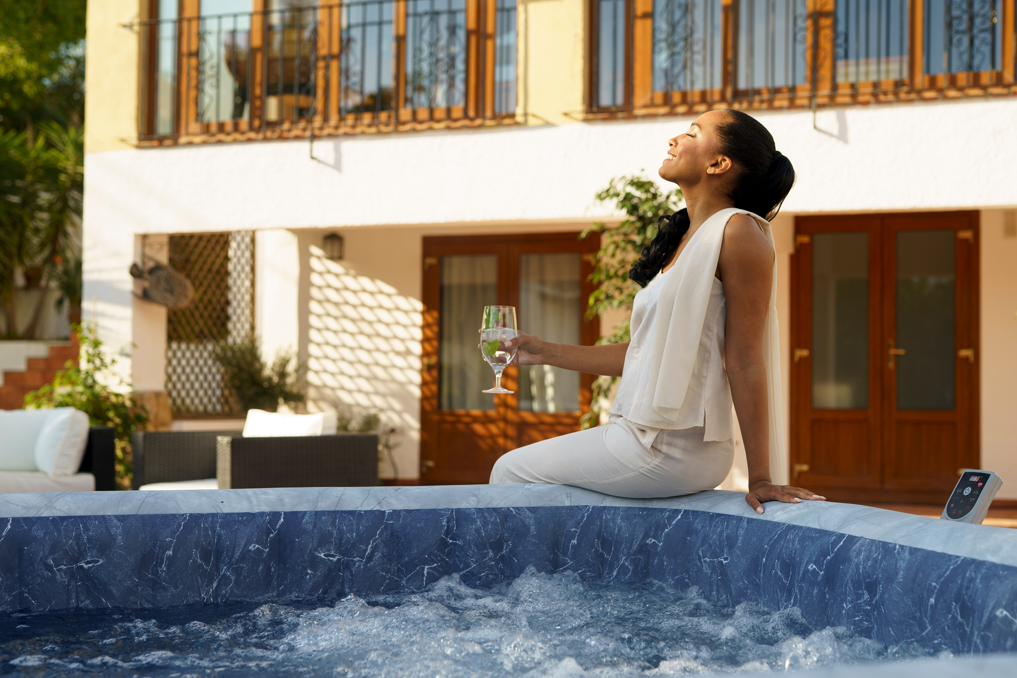 Frau sitzt am Whirlpool-Rand mit einem Glas Getränk in der Hand.