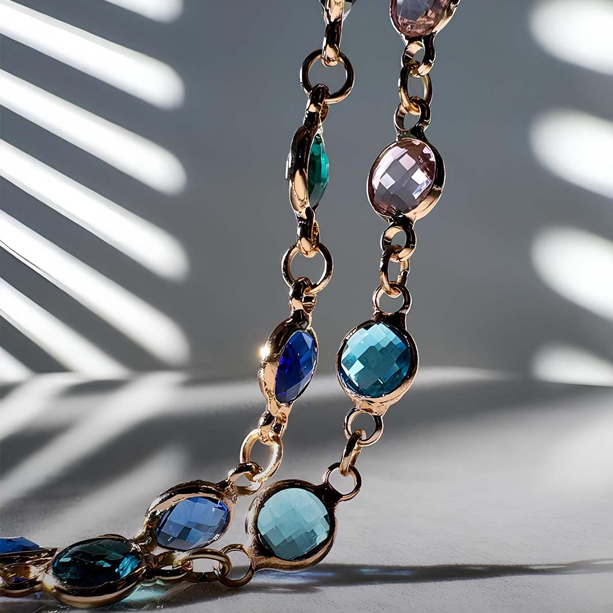 Goldkette mit bunten facettierten Steinen, vor gestreiftem Hintergrund.