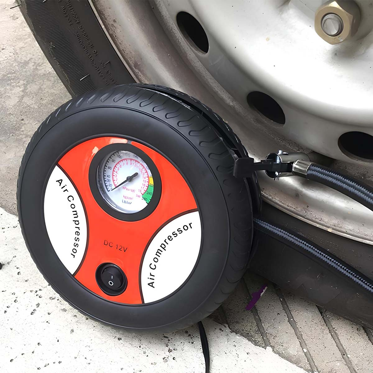 Ein tragbarer 12V Luftkompressor mit Manometer liegt neben einem Autoreifen.