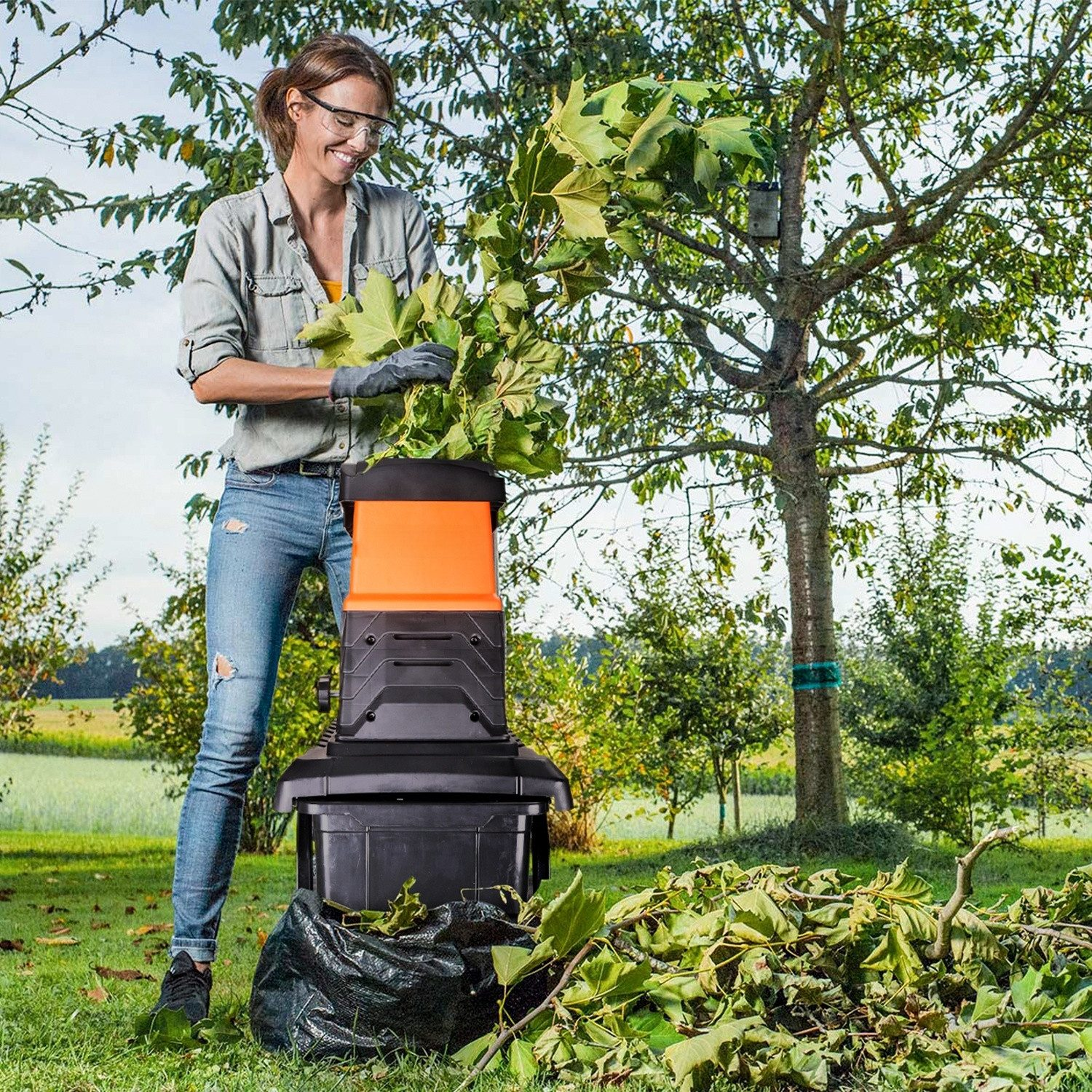 Frau schreddert Blätter in einem Garten mit einem elektrischen Häcksler.