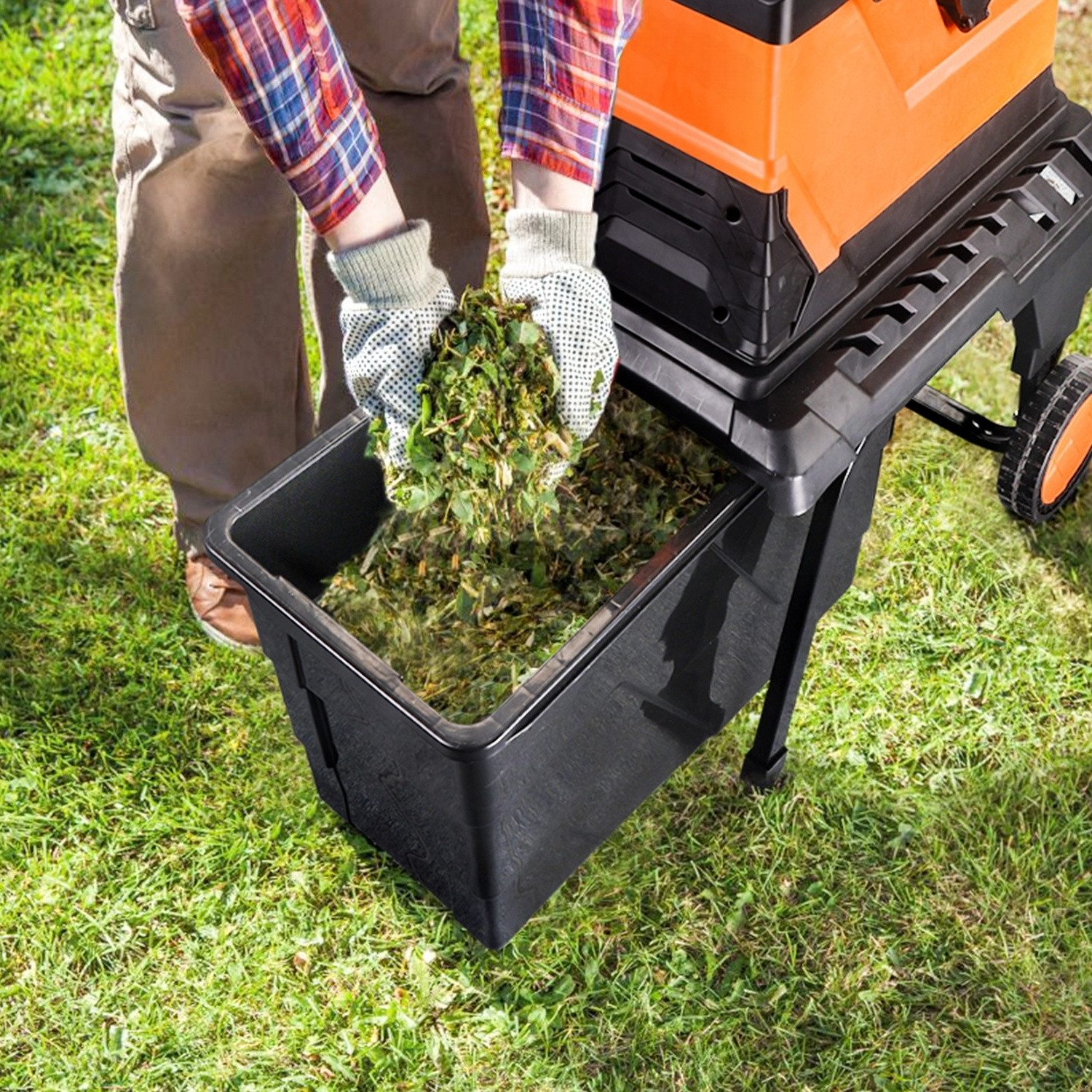 Mann füllt Häckselgut mit Handschuhen in eine schwarze Auffangbox einer Gartenhäckslermaschine.