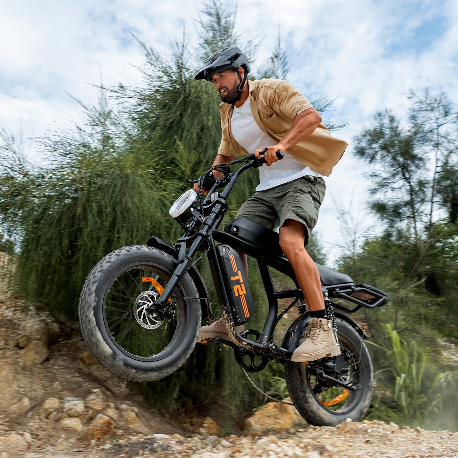 Mężczyzna jedzie rowerem elektrycznym w terenie, przednie koło w powietrzu, drzewa i niebo.