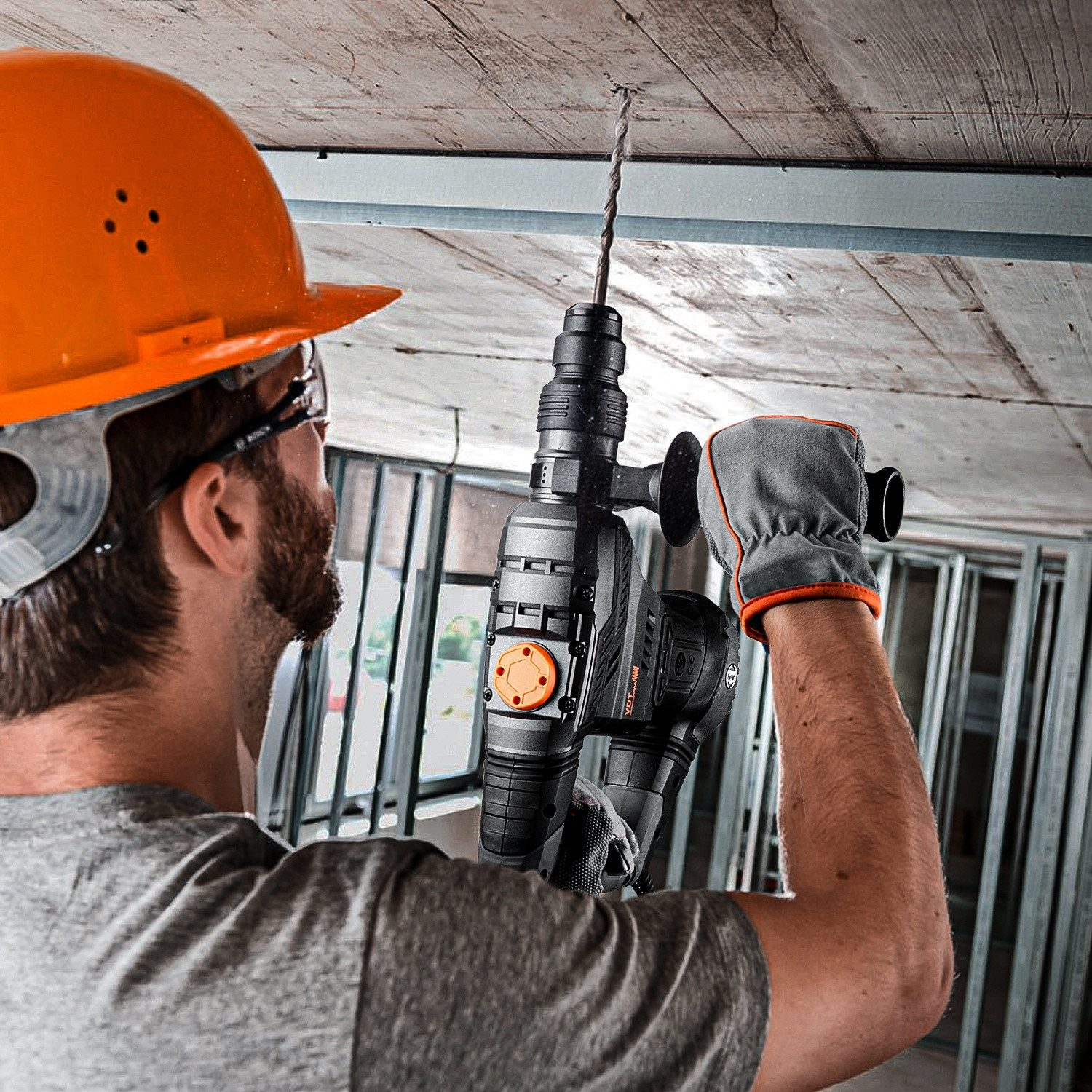 Ein Mann mit orangefarbenem Helm bohrt in die Decke eines Gebäudes.