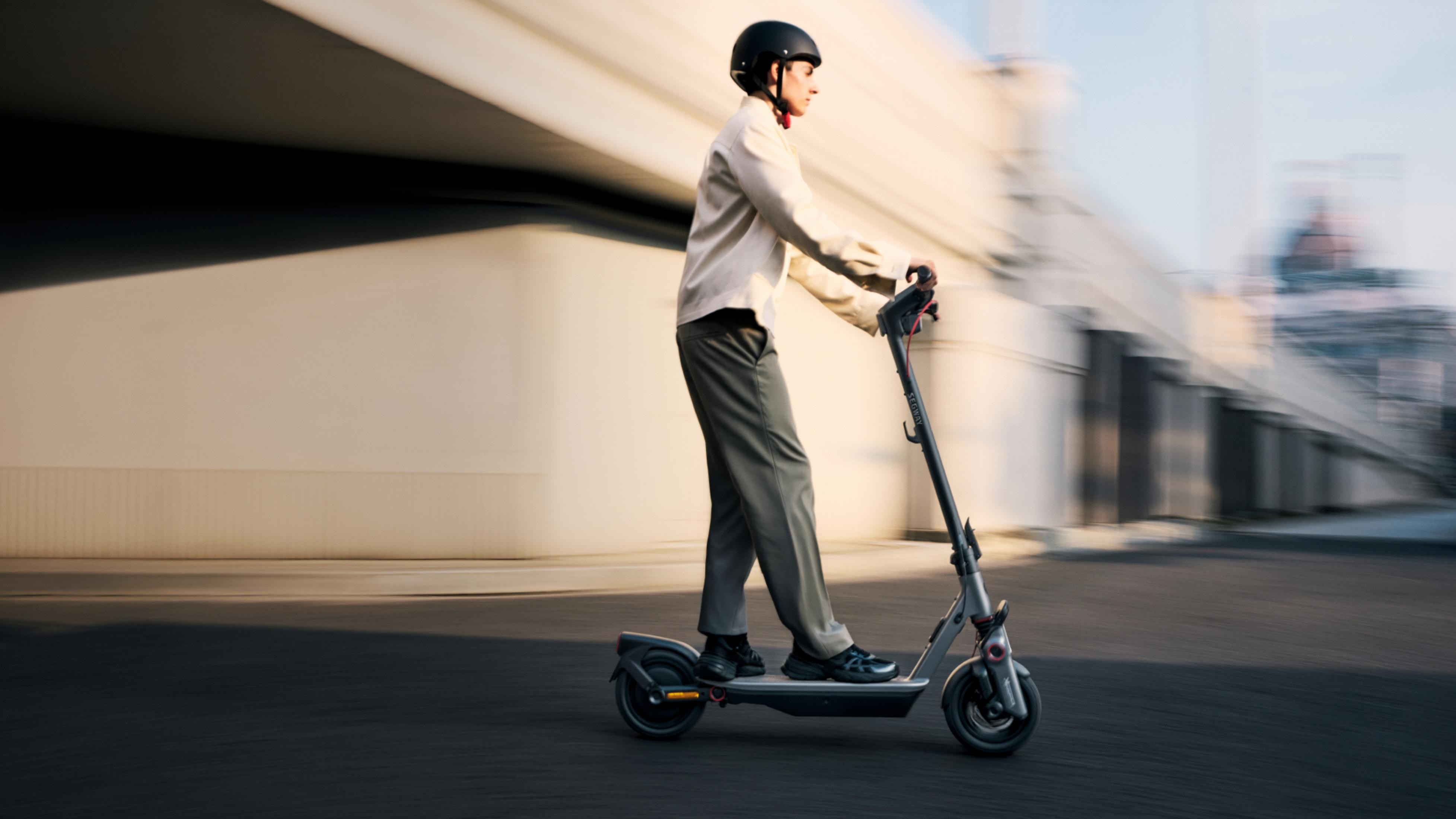 Ein Mann fährt einen E-Scooter unter einer Brücke. Er trägt einen Helm.