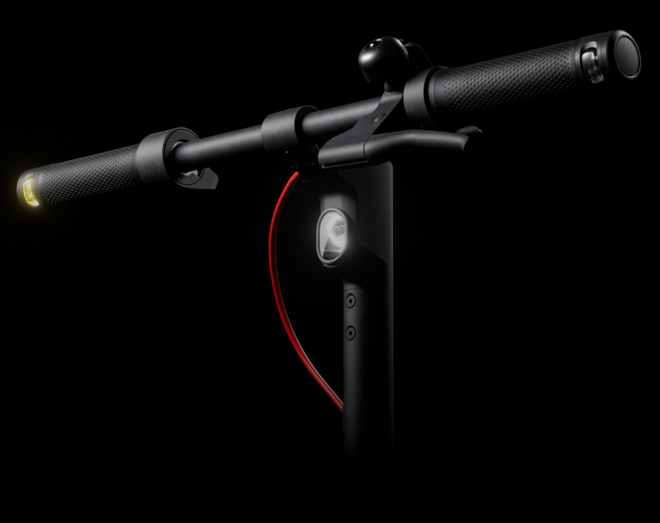Nahaufnahme des Lenkers eines schwarzen Elektrorollers mit Licht und rotem Kabel.