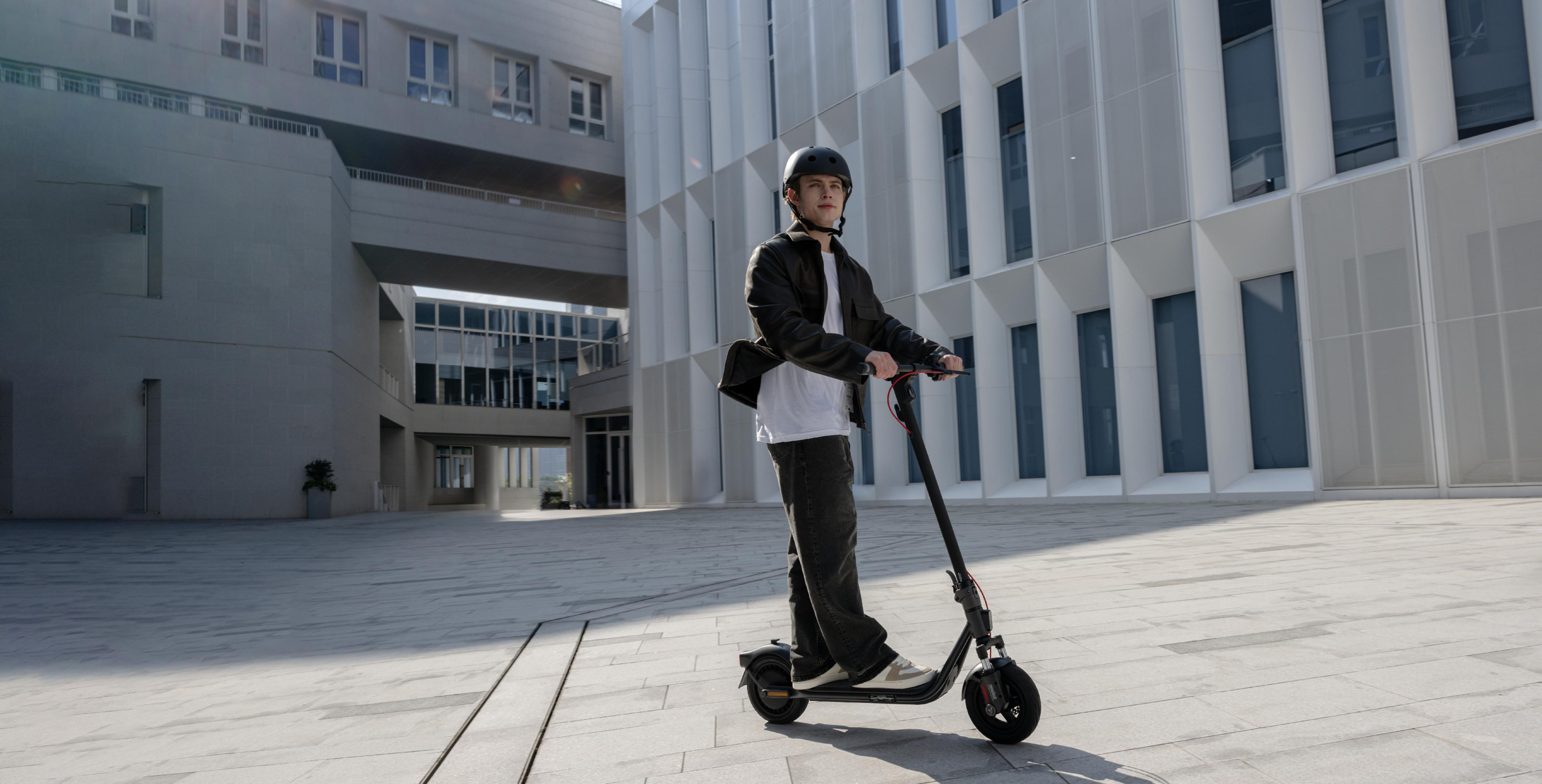 Ein Mann mit Helm fährt einen E-Scooter vor einem modernen Gebäude.