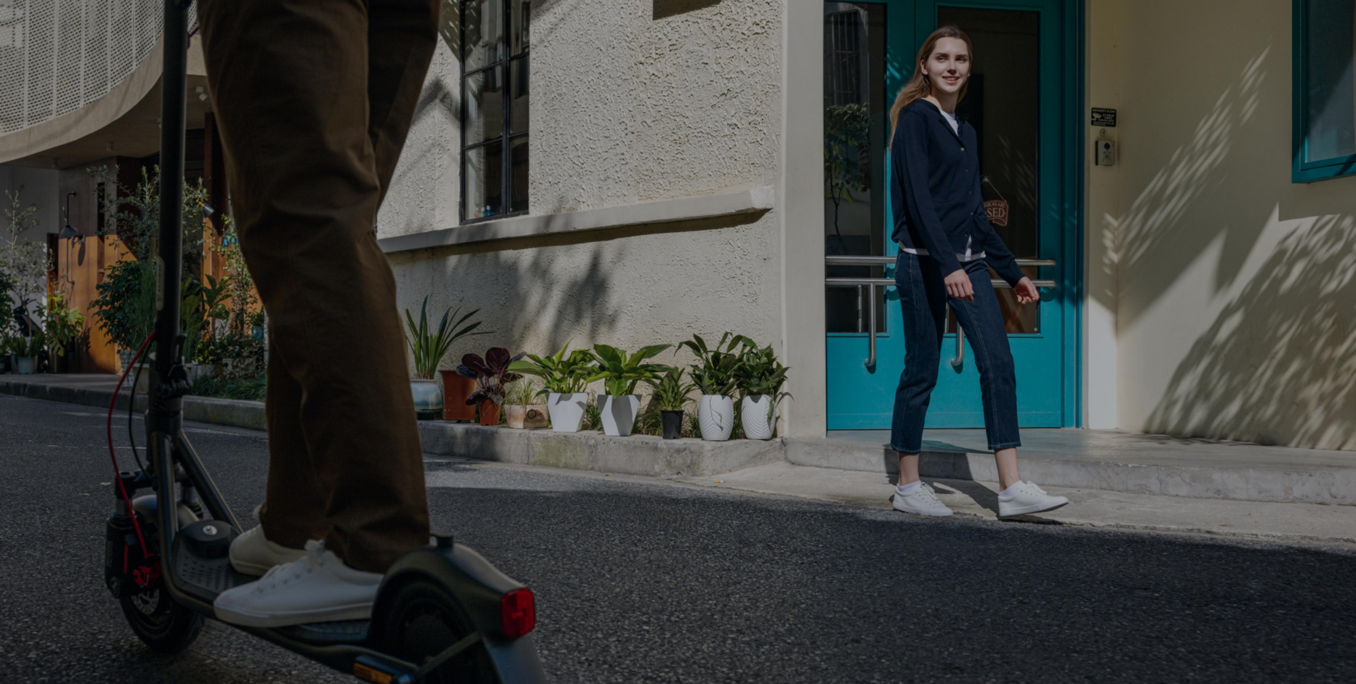 Eine Frau geht an Pflanzen vorbei, während jemand auf einem E-Scooter fährt.