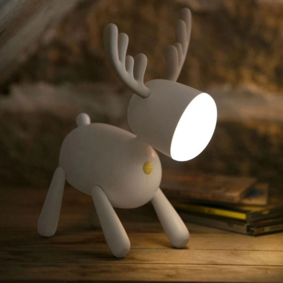 Eine weiße Rentierlampe mit leuchtendem Licht steht auf einem Holztisch.