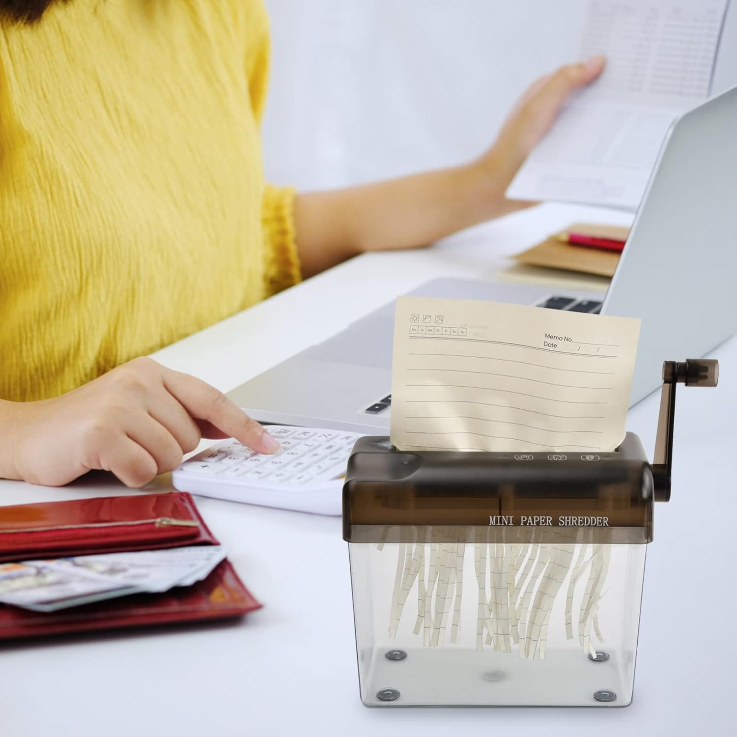 Person schreddert Papier mit Mini-Aktenvernichter, nutzt Taschenrechner & Laptop.