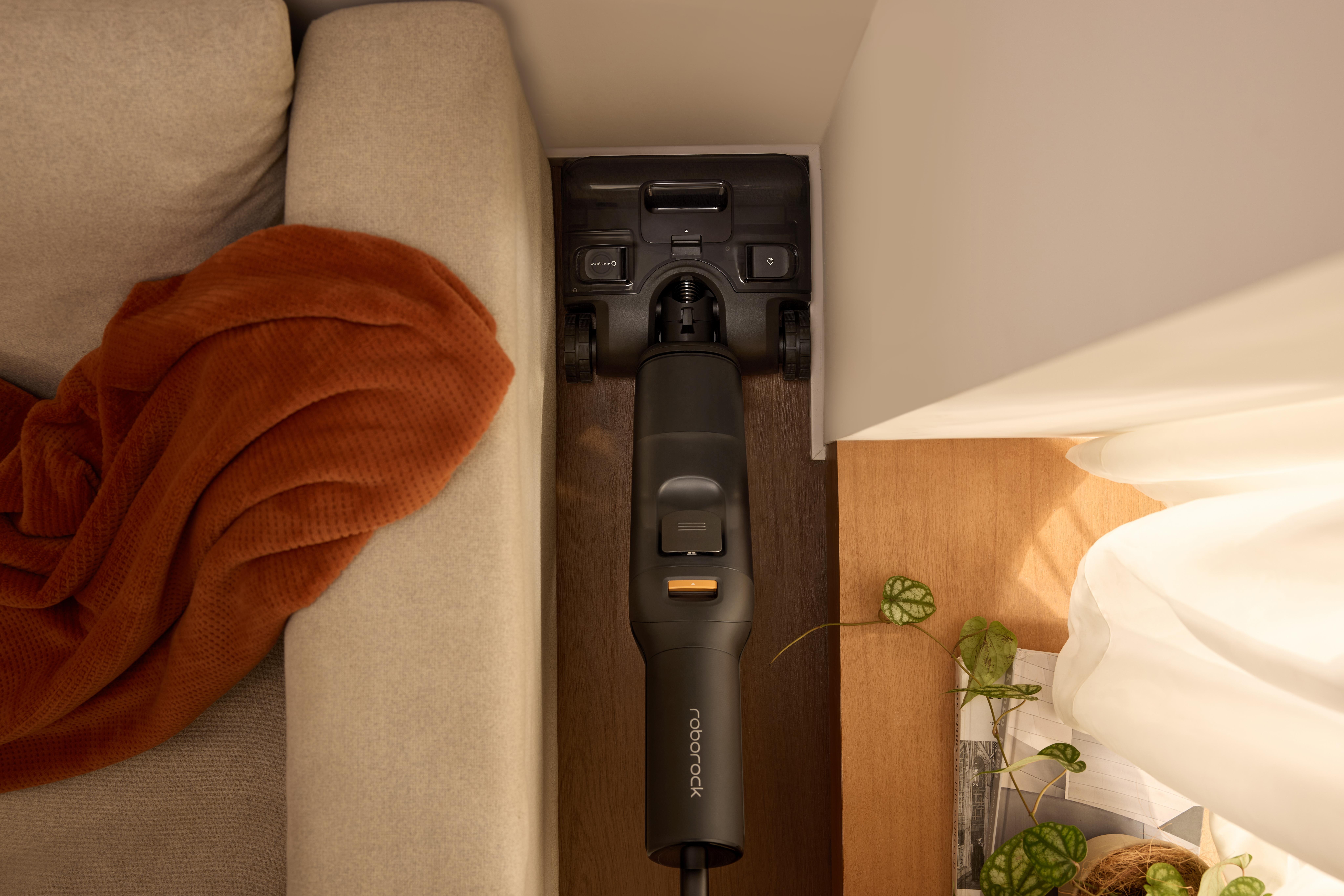 Czarny odkurzacz czyści między sofą a drewnianymi meblami.