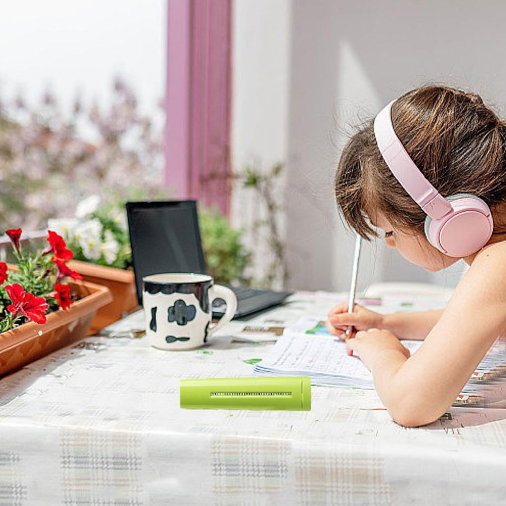 Kind mit Kopfhörern schreibt am Tisch. Laptop und Blumen im Hintergrund.