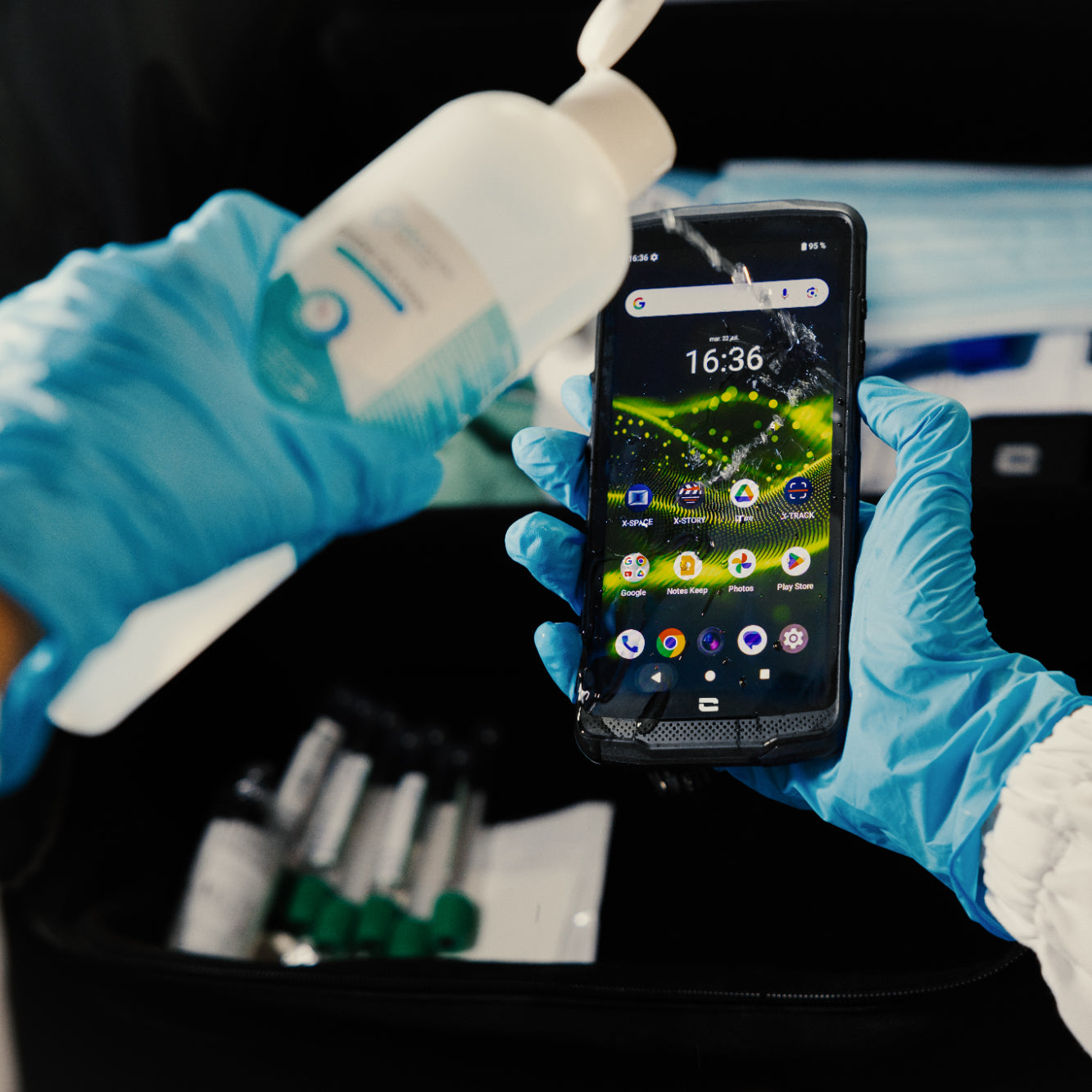 Handen in blauwe handschoenen houden een smartphone vast terwijl ze desinfectiemiddel erop gieten.