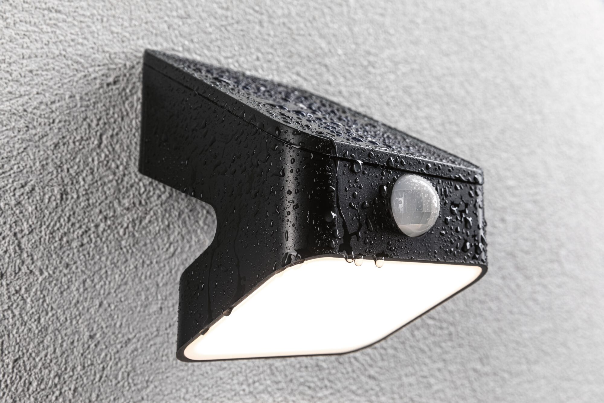 Czarna lampa zewnętrzna z czujnikiem ruchu, mokra od deszczu.