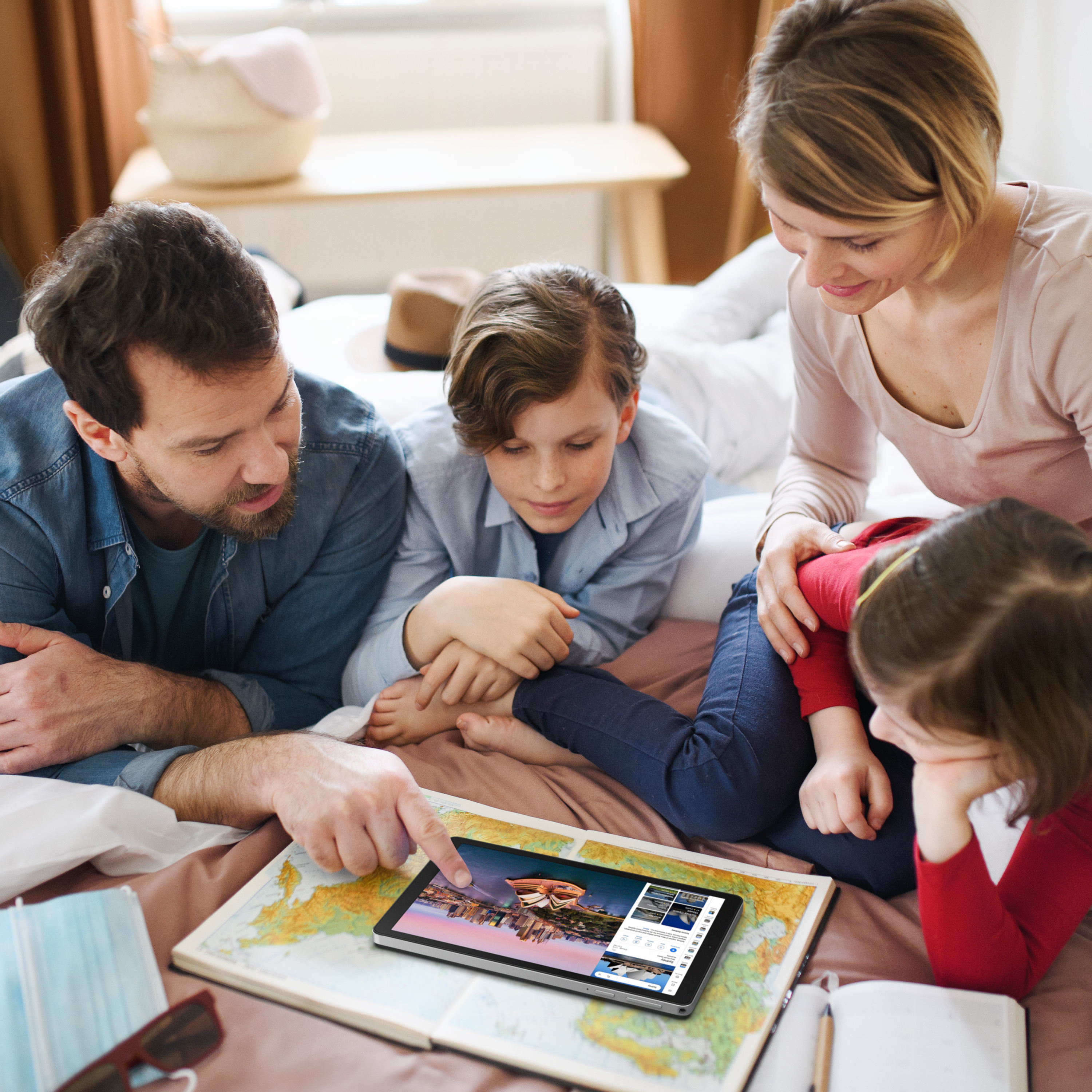 Rodzina planuje podróż z tabletem i mapą w łóżku.