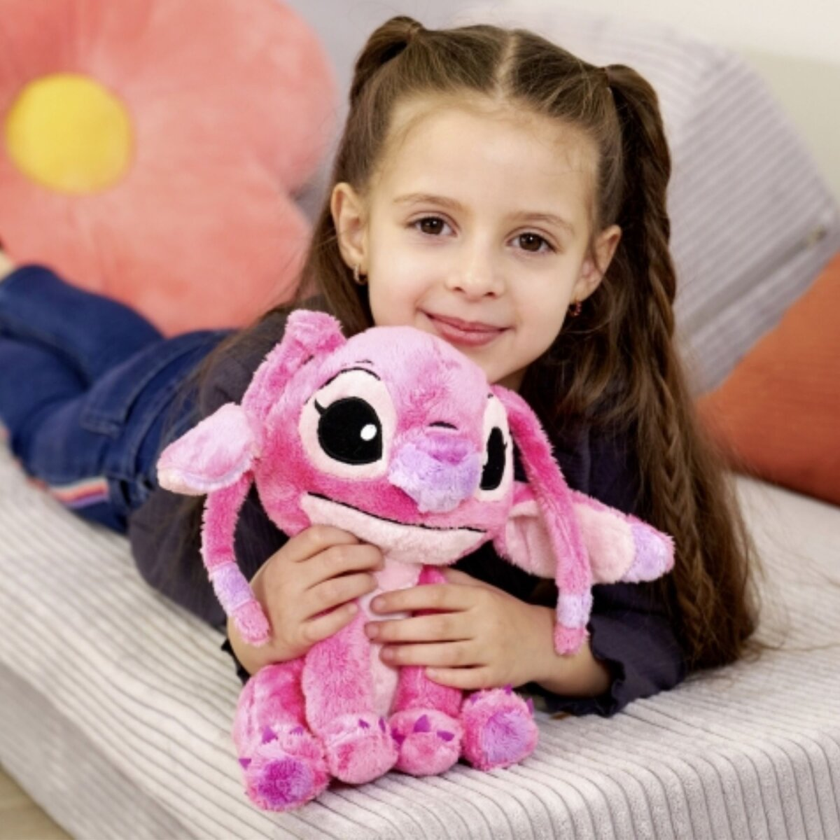 Une fille est allongée sur un lit, tenant une peluche rose de Stitch.