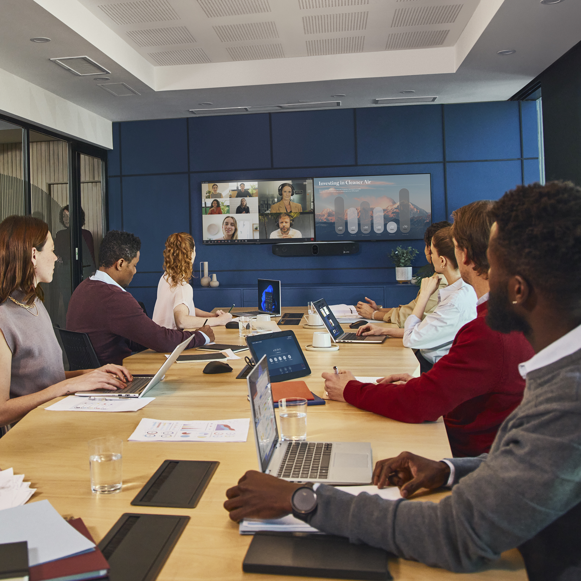 Persone in una sala riunioni con laptop e un grande schermo che mostra una videoconferenza.