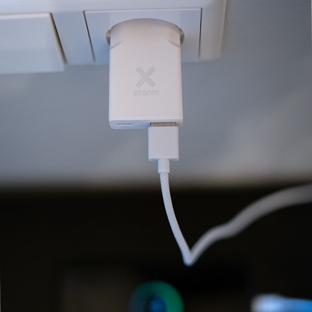 Un alimentatore bianco con logo Xtorm è inserito in una presa.
