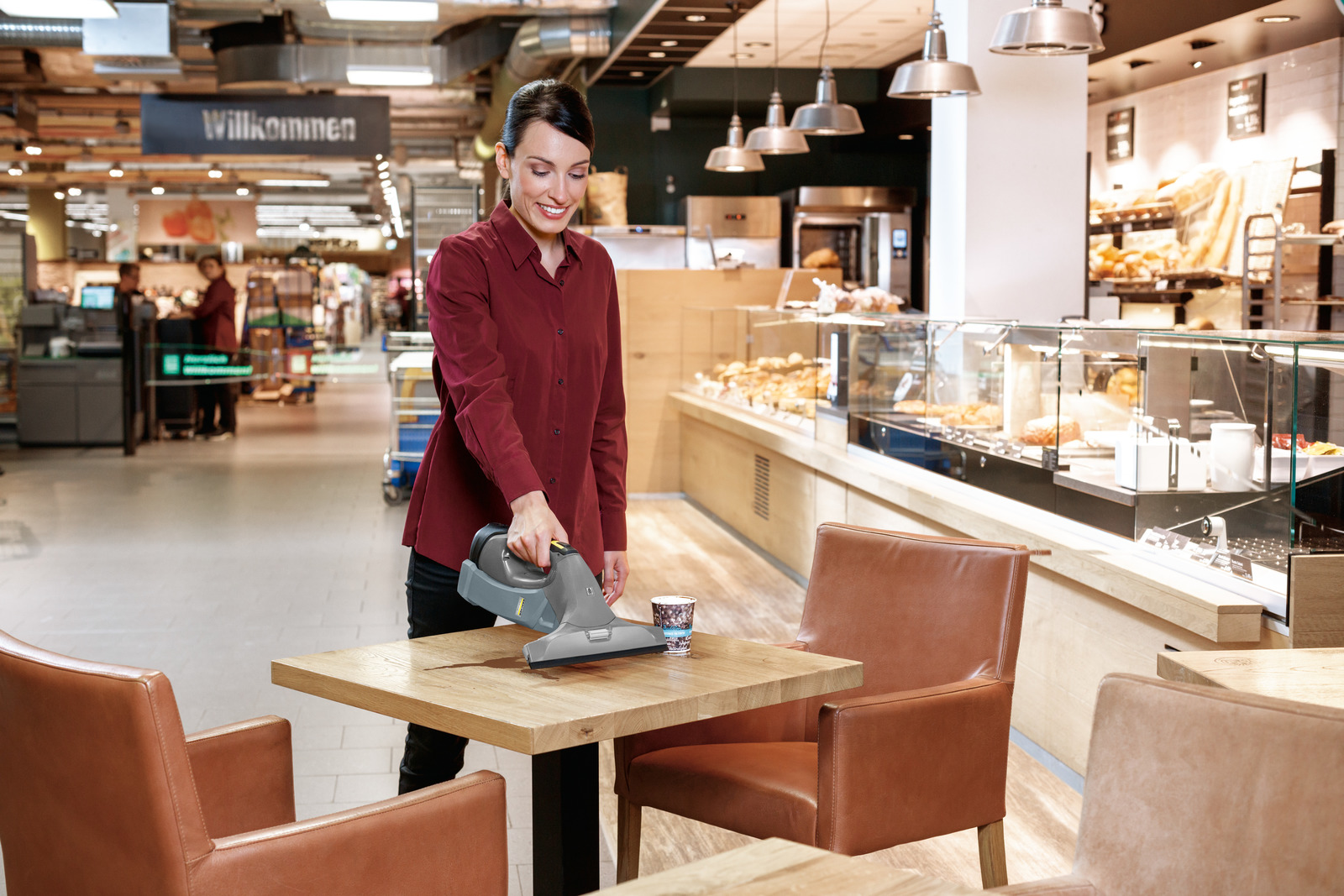 Une femme nettoie une table en bois avec un aspirateur à main dans un café.