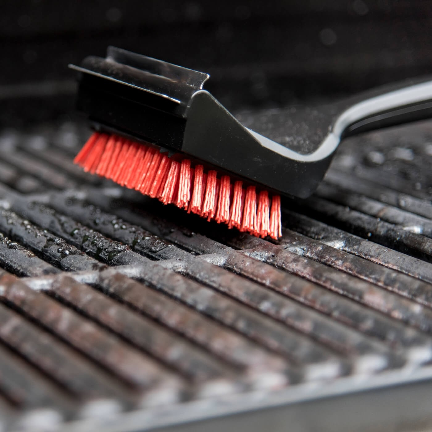 Ein roter Grillreiniger bürstet über schmutzige Grillroste.