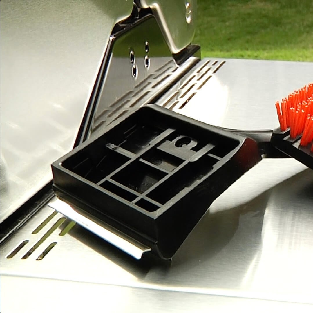 Ein Grillschaber mit orangefarbenen Borsten auf einem Grill.