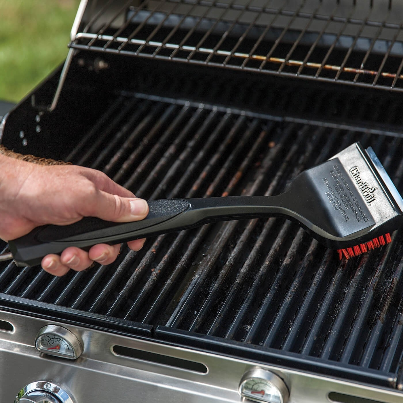 Ein Mann reinigt den Grillrost mit einer schwarzen Bürste mit roten Borsten.