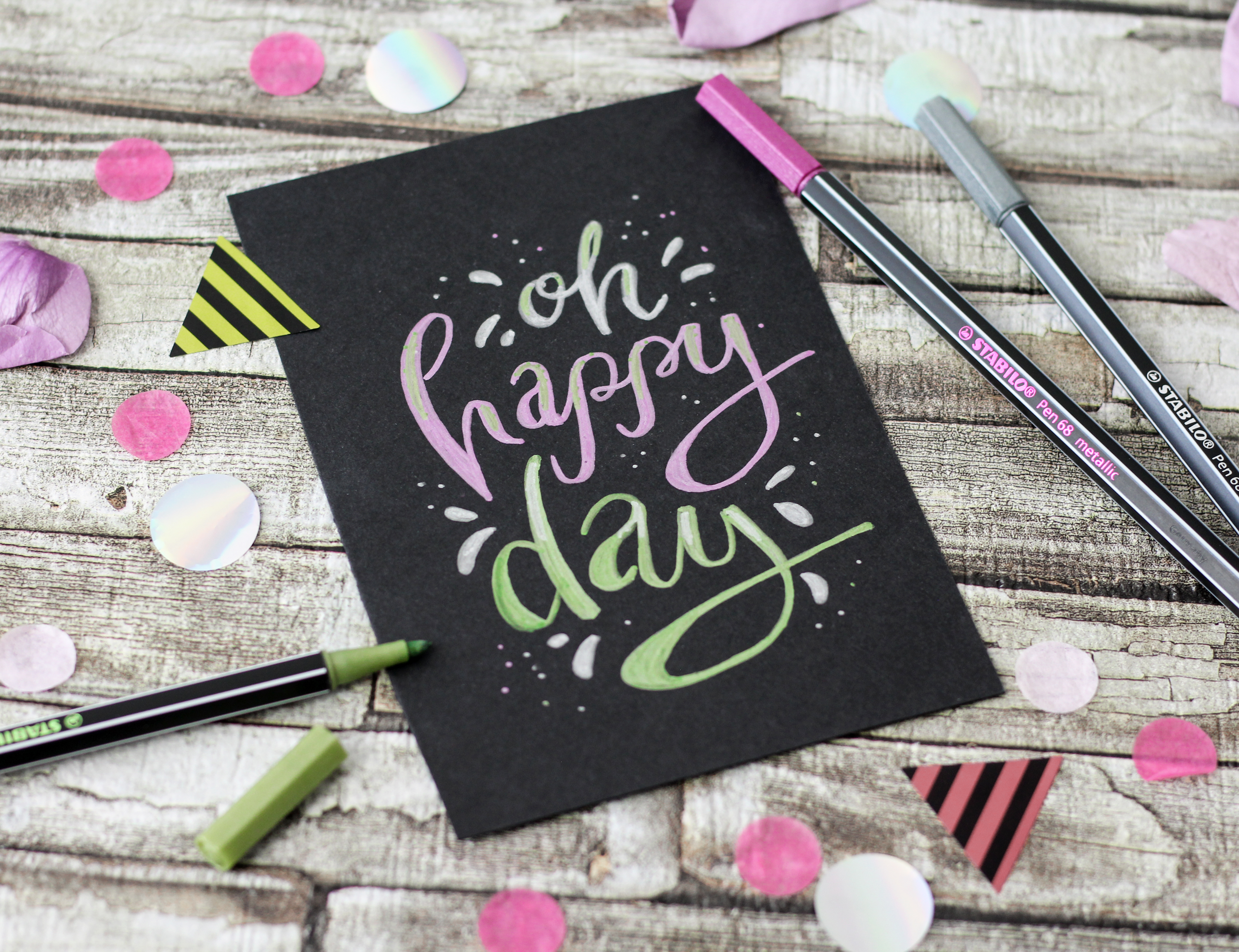 Biglietto nero con "Oh happy day" scritto in lettere colorate.