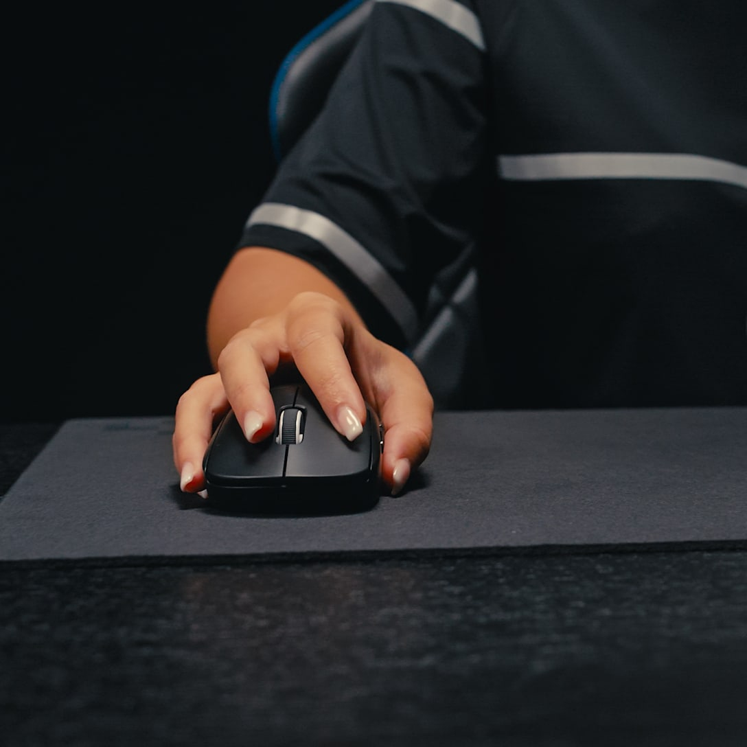 Une main utilise une souris noire sur un tapis de souris gris.