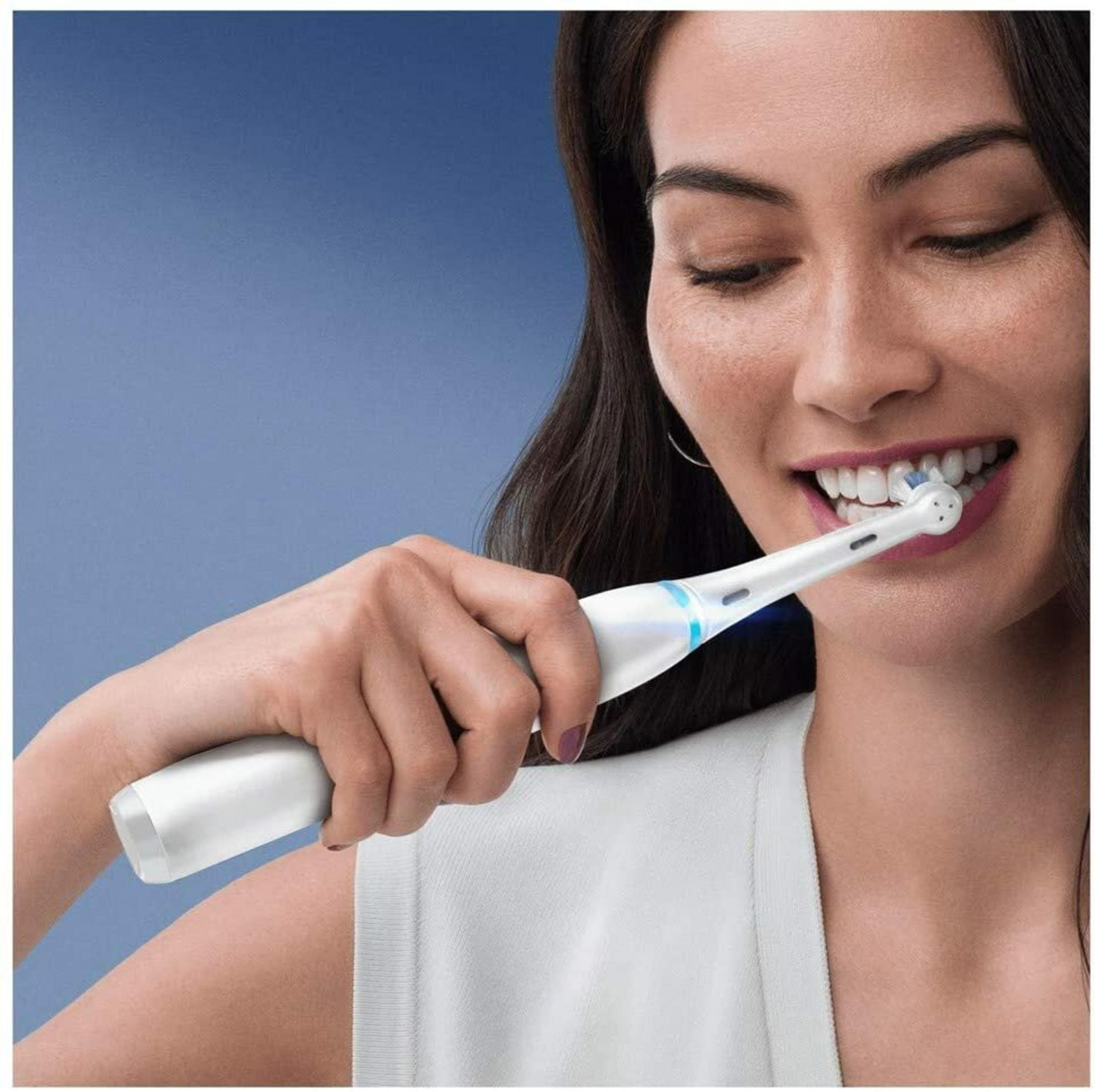 Una donna si lava i denti con uno spazzolino elettrico bianco.