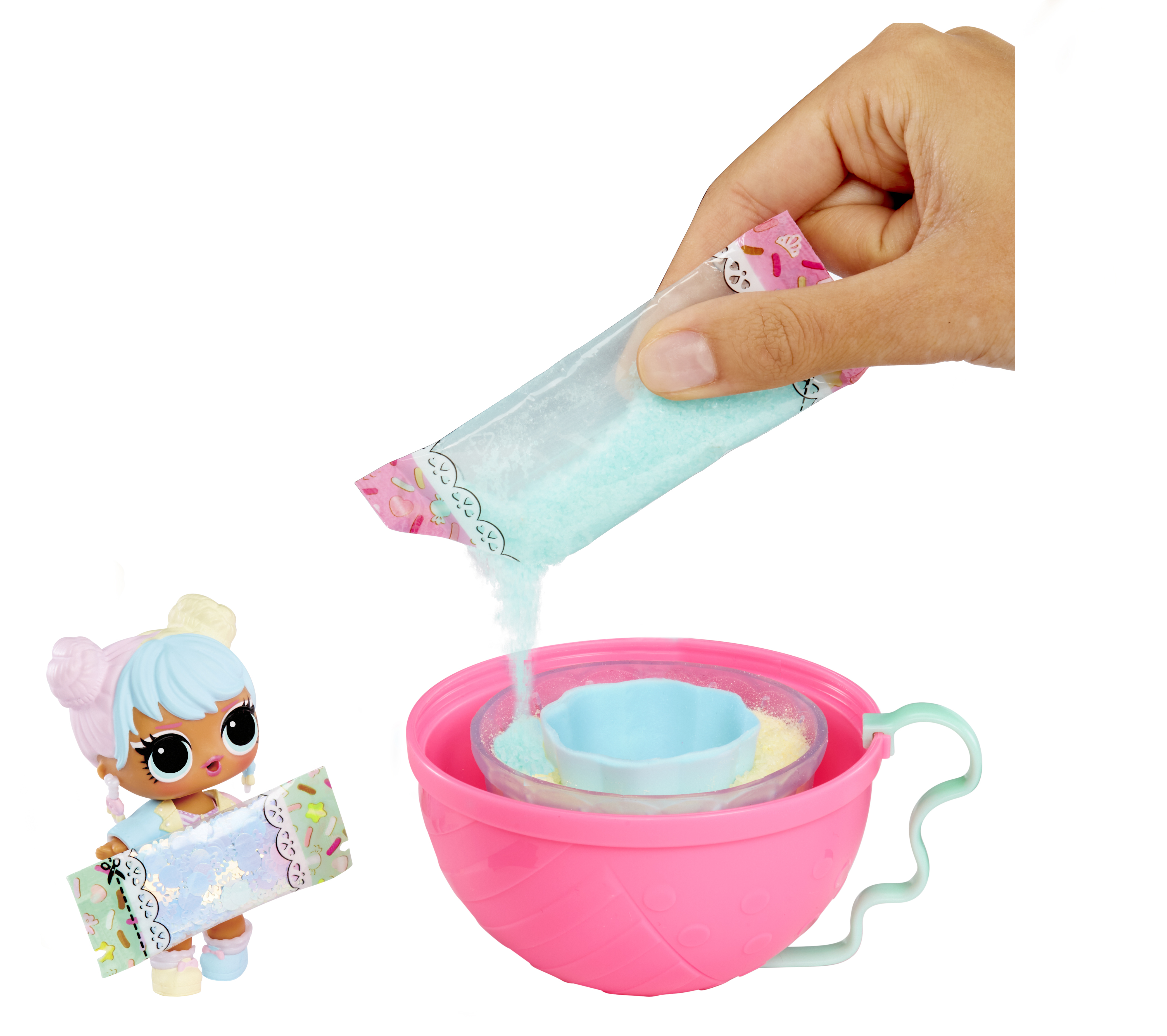 Una mano versa glitter azzurro da una bustina in una tazza rosa. Una bambola si trova a sinistra.