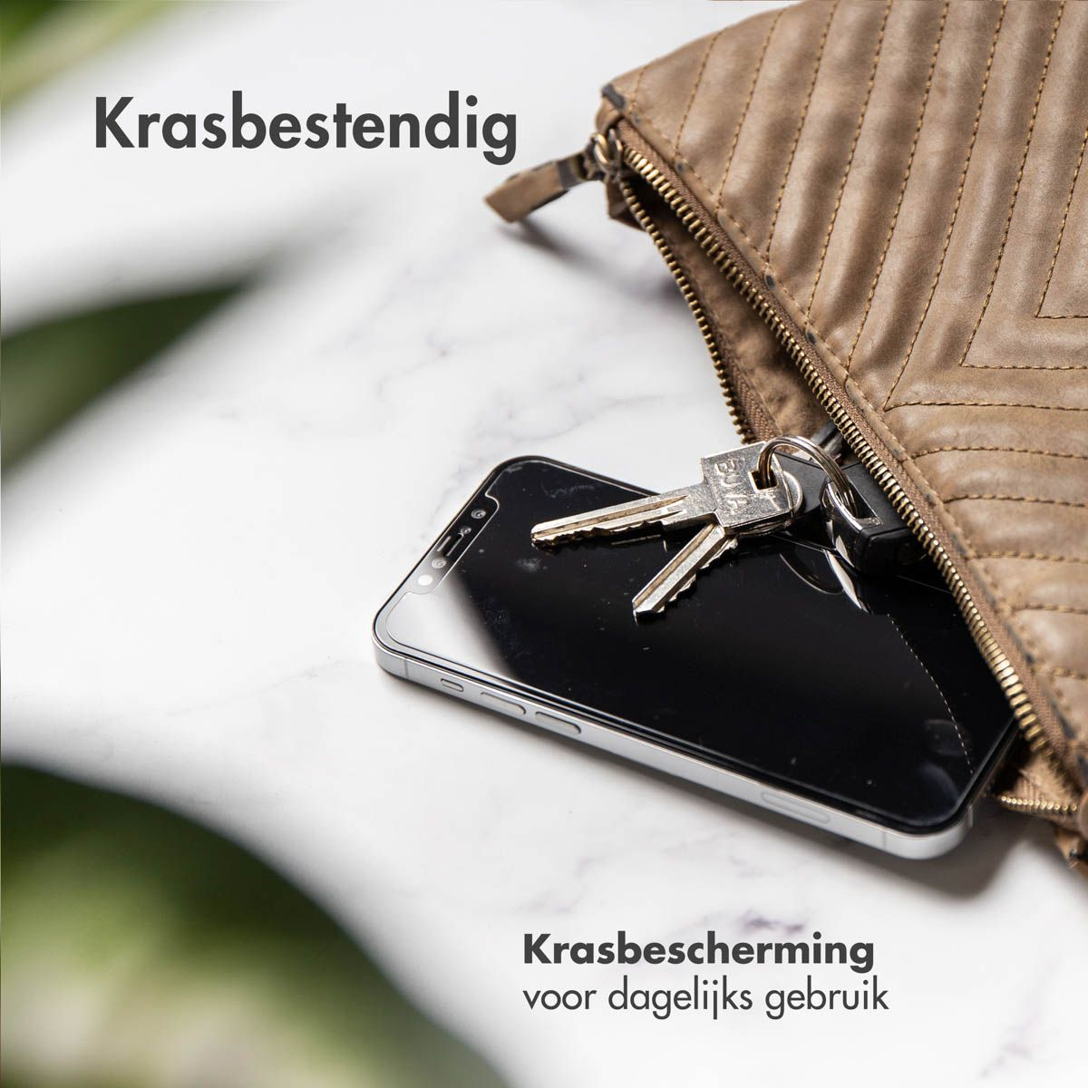 Een smartphone met sleutels in een bruine tas op marmer.