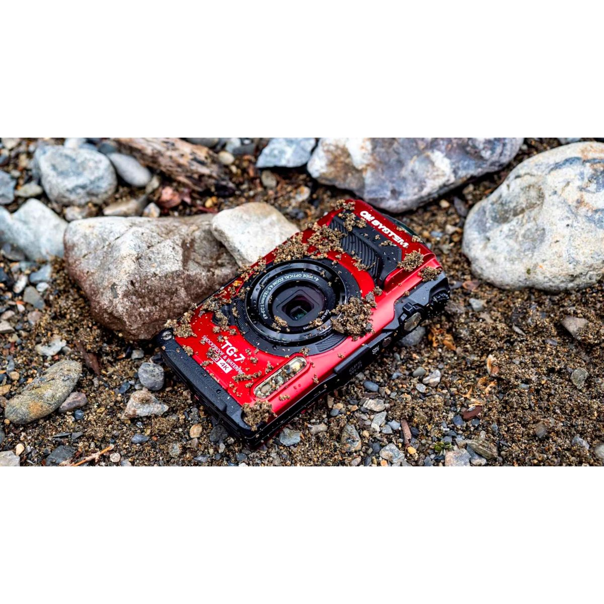 Una cámara digital roja yace sobre suelo arenoso con piedras.