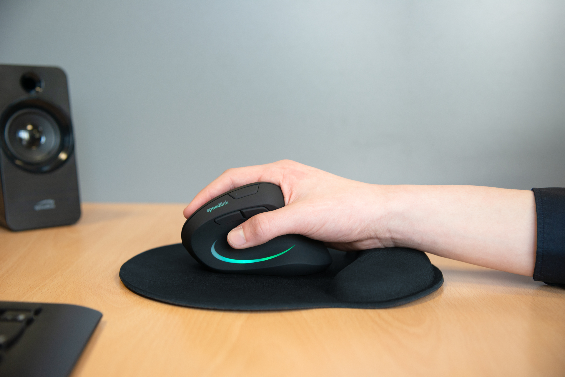 Een hand gebruikt een zwarte muis met blauwgroene verlichting op een muismat.
