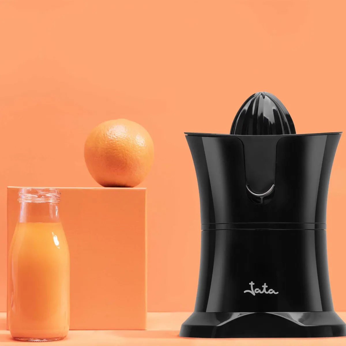 Schwarzer Entsafter mit Orange und Saftflasche auf orangefarbenem Hintergrund.