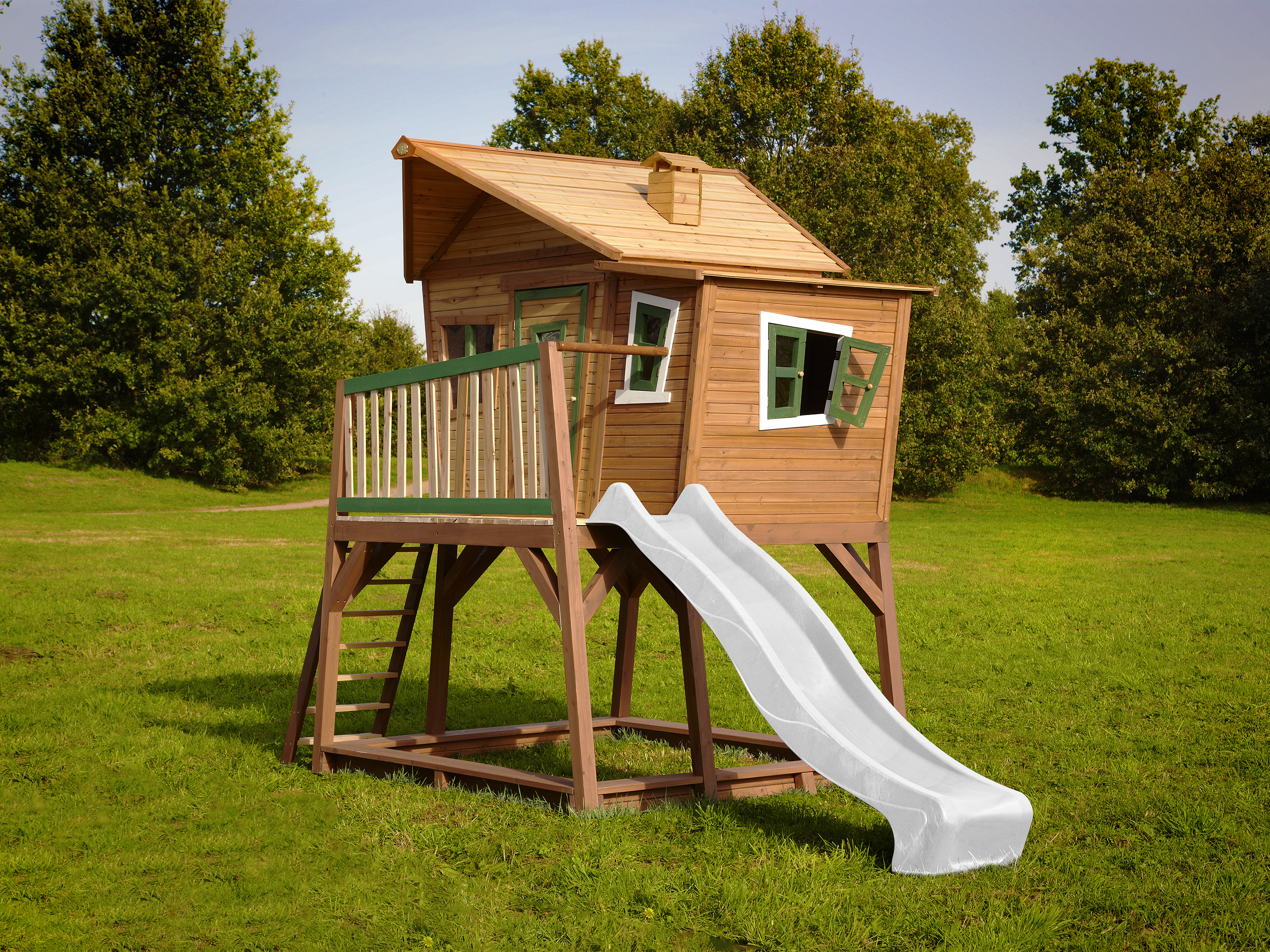 Ein Holzhaus auf Stelzen mit Rutsche und Leiter, umgeben von Grün.