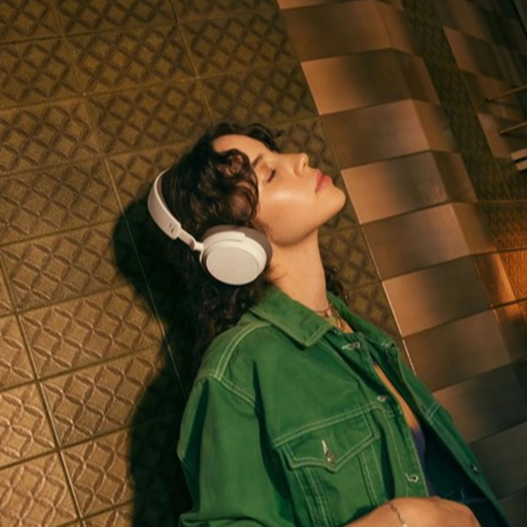 Kobieta w słuchawkach relaksuje się przy teksturowanej ścianie.