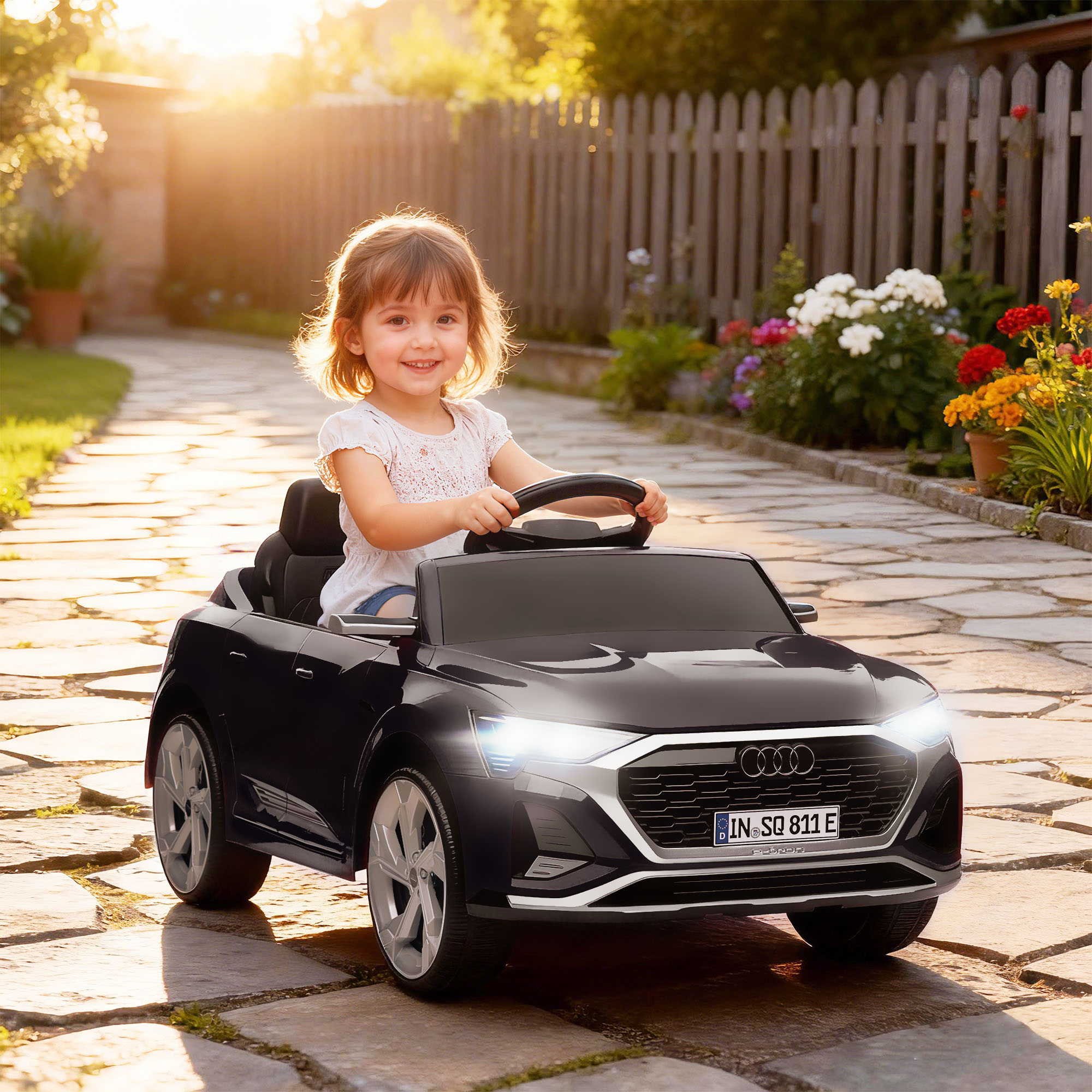 Una niña conduce un coche de juguete negro en un jardín al atardecer.