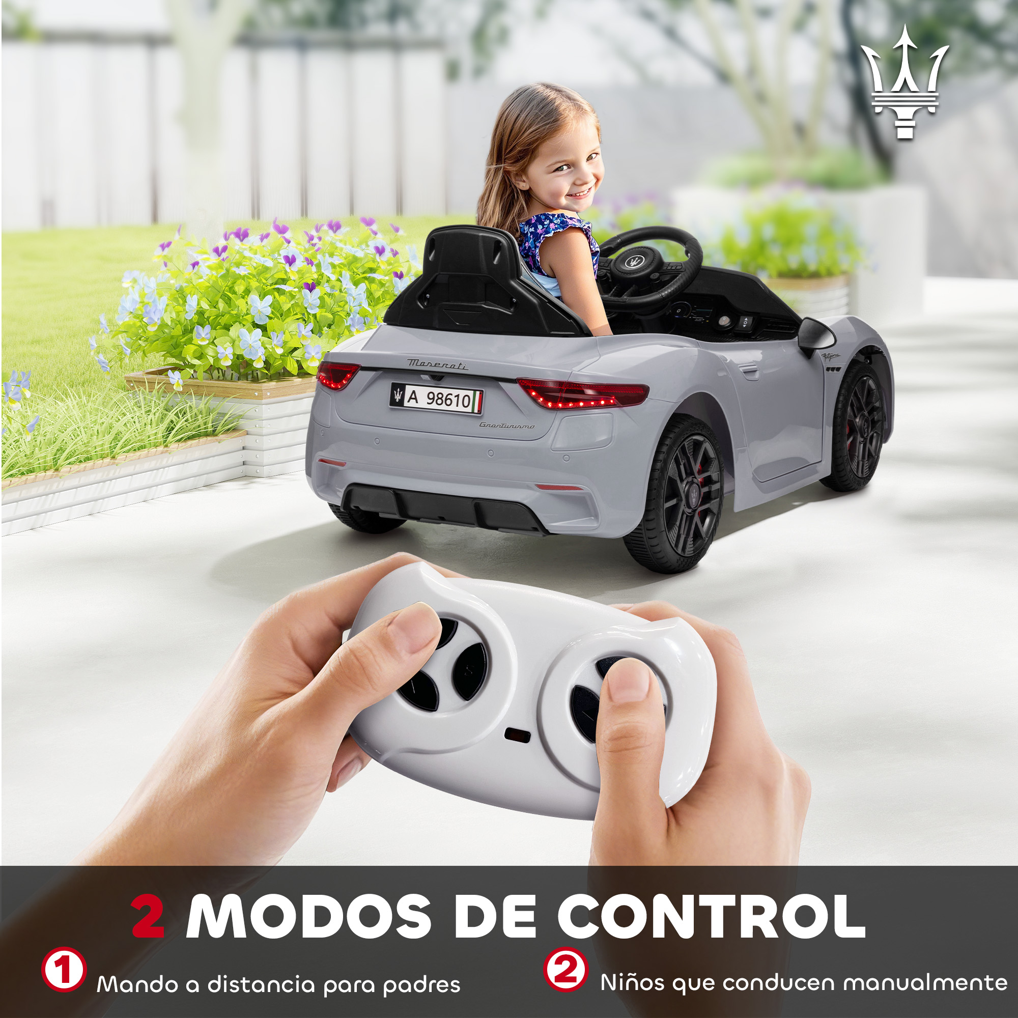 Una niña sentada en un coche de juguete Maserati gris. Una mano sujeta un mando.