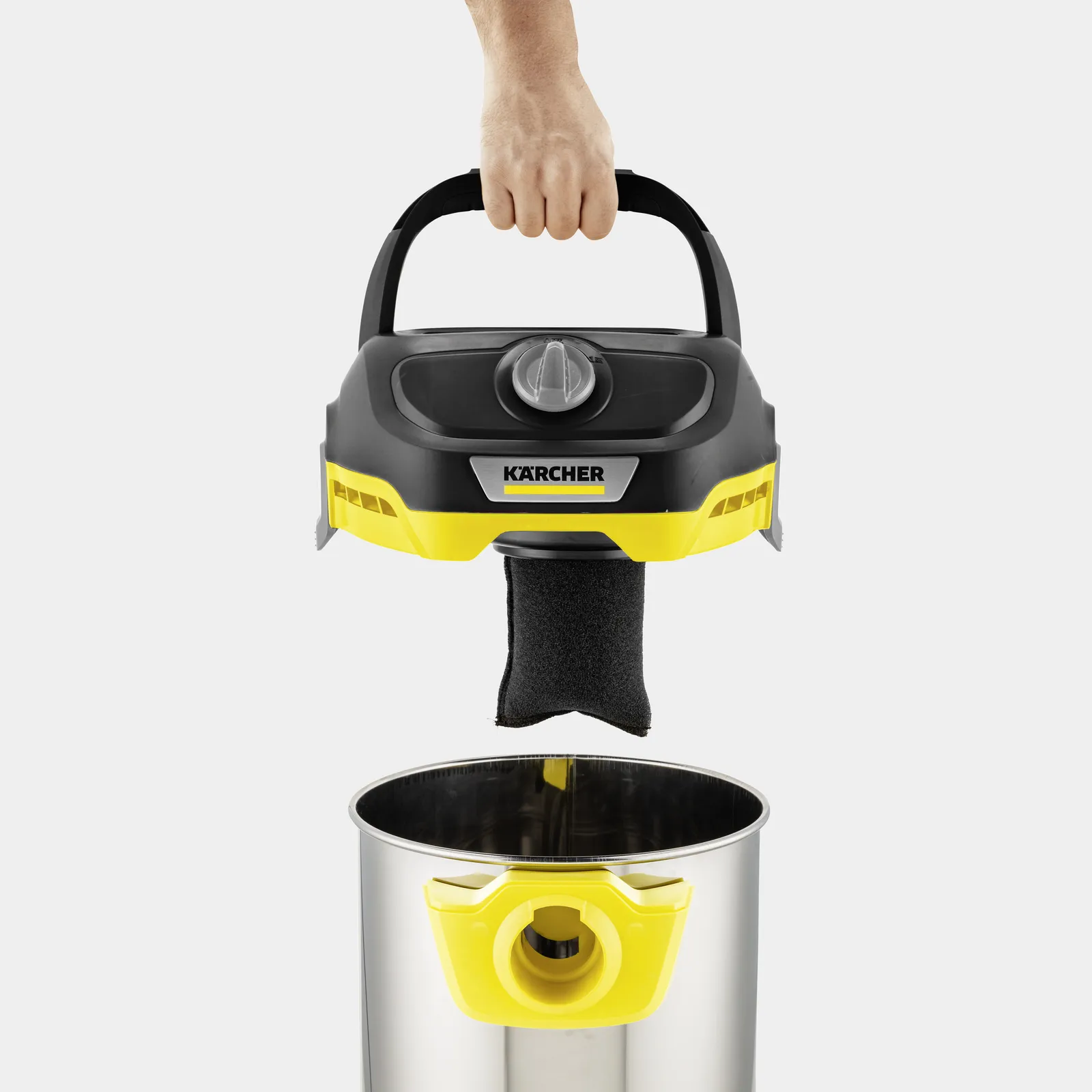 Dłoń trzyma czarną rączkę odkurzacza Kärcher. Filtr wisi nad metalowym pojemnikiem.